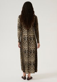 Largo vestido de estampado de leopardo en negro, beige y marrón, con mangas largas y corte recto. Lleva consigo unos zapatos negros de rejilla sin cordones.