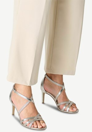 Silver high-heeled sandals with crisscross straps, featuring a metallic finish and a smooth texture, showcasing open toes and a slender heel.