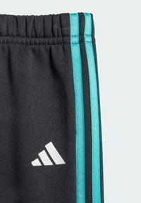 Pantaloni sportivi neri con strisce turchesi sui lati e un logo bianco. Realizzati in tessuto morbido con vita elasticizzata.