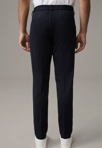 Męskie spodnie wykonane z ciemnogranatowej tkaniny o fakturowanej powierzchni, z elastycznym paskiem i przednimi kieszeniami. Połączone z białymi tenisówkami.