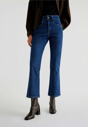 Blue high-waisted flared jeans made of denim, featuring a five-pocket design and subtle stitching details. Worn with brown block-heeled boots.