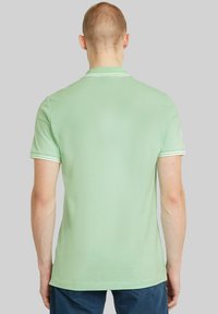 Grön pikétröja med en slät textur, med korta ärmar och en kontrasterande vit krage och ärmavslut. Standard passform.