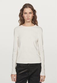 Long-sleeve cream shirt with a round neckline, soft texture, fitted design, paired with dark corduroy pants. Simple and versatile style.