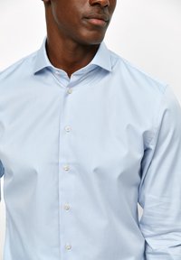 Lichtblauwe overhemden met een gladde stof, voorzien van een klassieke kraag, lange mouwen en witte knopen aan de voorkant.