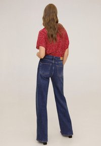 Wijde blauwe denim jeans met hoge taille, twee achterzakken, gecombineerd met een kortekorte mouw rode blouse met witte stippen.