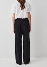 Zwarte wijde broek gemaakt van een zachte stof, met een elastische tailleband en twee achterzakken, met een gladde, matte textuur.