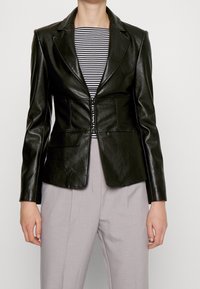 Černý imitace kůže blazer s přiléhavým střihem, klopami a dvěma předními kapsami, přes pruhované tričko a světle šedé kalhoty.