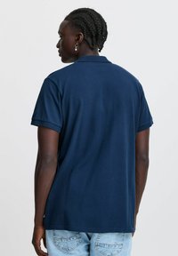 Navy modra polo majica iz bombaža, s kratkimi rokavi, ribastim ovratnikom in ravnim robom. Zadnji pogled, brez vidnih vzorcev ali logotipov.