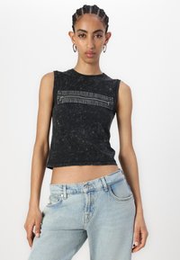 Svart ärmlös crop top med en strukturerad yta och en horisontell dragkedjeficka över bröstet; matchad med ljusblå denimjeans.