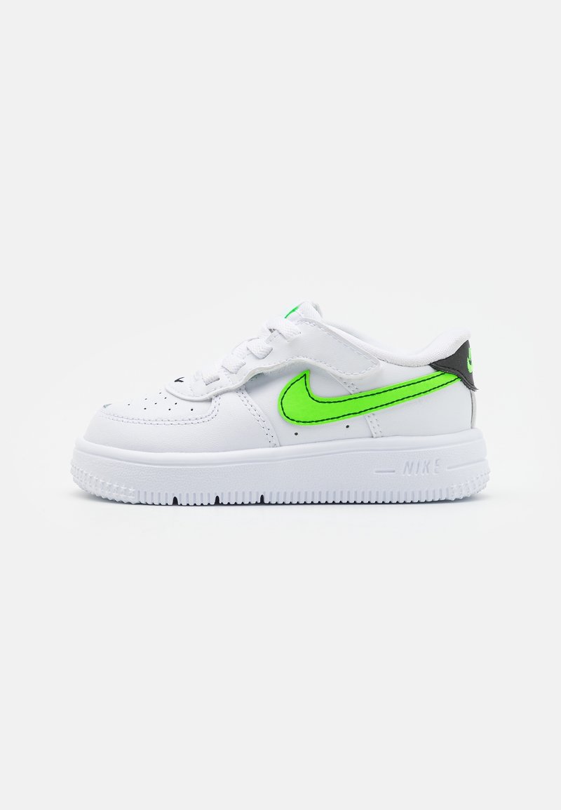 Baskets blanches Nike avec un swoosh vert vif et des accents noirs, design bas et semelle texturée visible de côté.