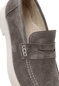 Zapato gris de ante tipo slip-on con una tira ancha en el empeine, acentos de costura blanca y una suela de goma. Forro interior liso visible.
