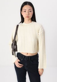 Cream ribbed cropped sweater with long sleeves. Paired with dark denim jeans and a small brown crossbody bag. Smooth texture, relaxed fit.