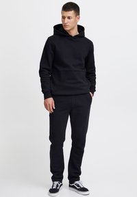 Juodas džemperis su gobtuvu ir laisvalaikio kelnės iš minkšto medvilnės mišinio. Džemperyje yra priekine kišenė, o kelnės pasiūtos siauro kirpimo. Juodi sportbačiai užbaigia įvaizdį.