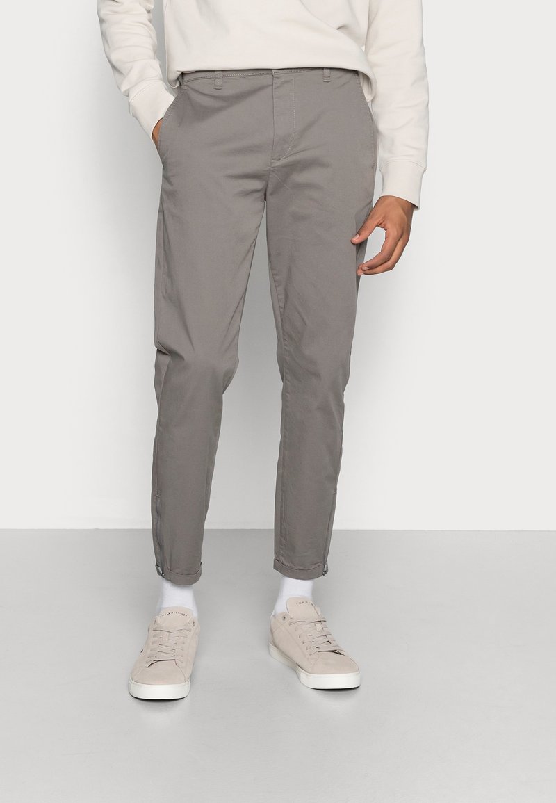 Chinos gris en mélange de coton avec une coupe fuselée et des poches latérales. Des baskets décontractées beige complètent la tenue. Design simple et épuré.
