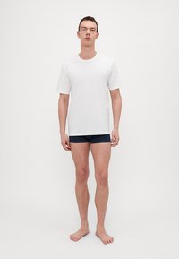Hvit T-skjorte med kort erm og rund hals, kombinert med mørkeblå boxershorts. Tøyet ser glatt og tettsittende ut, med et enkelt design.
