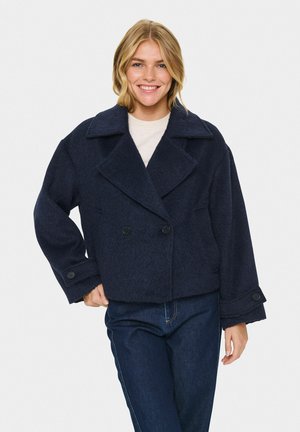 Giacca doppiopetto in misto lana blu navy con ampio colletto, grandi bottoni e vestibilità rilassata. Tessuto strutturato e lunghezza cropped.