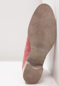 Semelle d'une chaussure en daim rose avec la taille 37 estampillée sur la semelle en caoutchouc, affichée à la verticale sur un fond blanc.