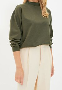 Olivgrön kort sweatshirt med hög krage och långa, något puffiga ärmar. Mjuk tyg med inga synliga mönster eller detaljer.