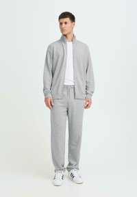 Sweat-shirt gris à fermeture éclair et pantalon de survêtement assorti en tissu doux. La tenue comprend des poignets élastiques et une taille à cordon. T-shirt blanc inclus.