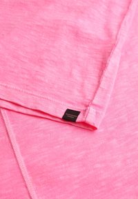 Camiseta de manga corta rosa, hecha de una tela suave, con una superficie ligeramente texturizada y una etiqueta de marca negra en el dobladillo.