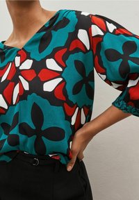 Blusa a maniche corte con un vivace motivo floreale in rosso, bianco e turchese su uno sfondo nero, dal taglio comodo e design con scollatura a V.