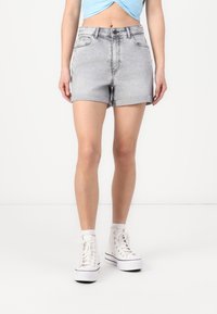 Bermuda in denim grigio con orli arrotolati, design standard a cinque tasche e chiusura con bottone in metallo, abbinati a sneakers bianche alte.