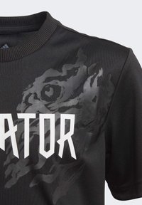 Černé tričko s texturovaným designem oka a drápu dravce, s odvážným bílým textem "RAPTOR" napříč hrudníkem, krátký rukáv a žebrovaný límec.