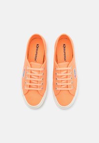 Orange canvas sneakers with white rubber soles, round toe, and flat laces. Features branding on the tongue and side panel.