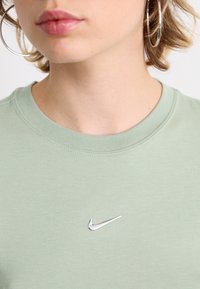 Világoszöld pamut póló kerek nyakkivágással. Ezüst Nike logóval a mellrészen. Simább textúra és laza dizájn.