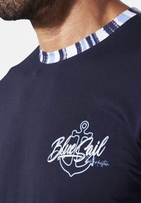 Navy T-shirt with a striped collar, featuring a white anchor logo and "BlueSail" text in a handwritten style on the front.