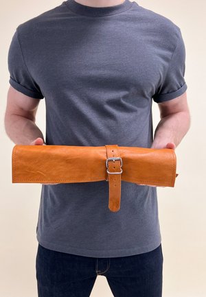 Hnědá kůže rolovací pouzdro s plochým designem, stříbrnou sponou a popruhem na zavírání. Povrch má hladkou texturu a minimální prošití.
