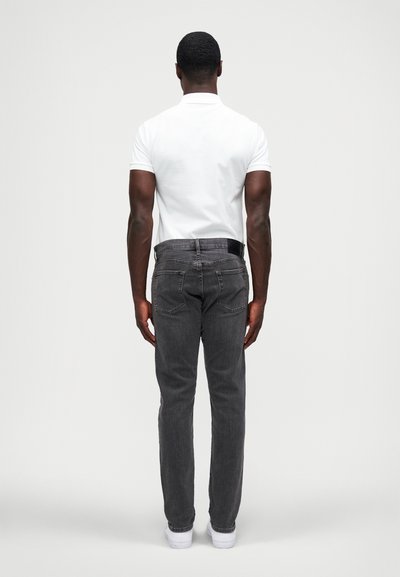 Jeans de ganga cinza com um corte standard, ligeira elasticidade e um design clássico de cinco bolsos, combinados com uma camisa polo branca ajustada.