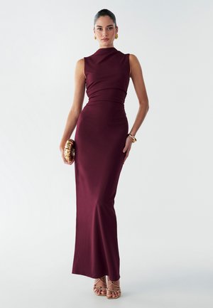 Burgundy iltavaate ilman hihoja, jossa on tiukka siluetti, korkea kaula-aukko ja kerätty kangas. Yhdistetty kultasävyisten asusteiden ja sandaalien kanssa.