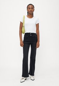 Valkoinen ribbikuvioinen lyhythihainen paita, korkeavyötäröiset mustat leveälahkeiset farkut, vihreä olkalaukku ja valkoiset kengät hopeisilla yksityiskohdilla.