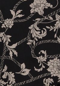 Tessuto nero con motivo floreale beige chiaro, caratterizzato da vigneti e foglie che si avvolgono, creando un design elegante e testurizzato.