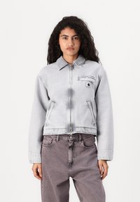 Lys grå denimjakke med glidelås, klassisk krage, frontlomme og senkede skuldre. Kombinert med grå denimbukser.