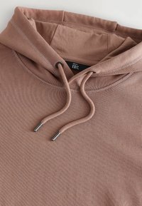 Dusty pink hoodie made from textured fabric, featuring a drawstring with metal tips and a ribbed neck. Label reads "NEXT EDIT."