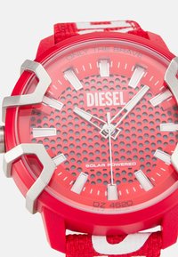 Red solar-powered watch featuring a textured dial with perforations, silver hour markers, and a durable rubber strap with a patterned accent.