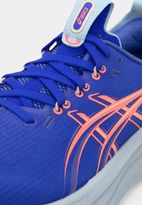 Niebieski but sportowy z teksturowanego materiału, z różowymi akcentami, amortyzowaną podeszwą i sznurowanym zapięciem. Wyraźne logo Asics na języku.