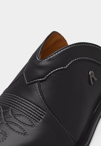 Μαύρο δερμάτινο παπούτσι τύπου slip-on με λευκή ραφή, διακοσμητική κεντητή στο μπροστινό μέρος και μικρό λογότυπο "R" στο πλάι.