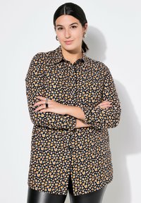 Zwarte button-up shirt met een oranje en crèmekleurig hartpatroon, lange mouwen en een ontspannen Pasvorm, gecombineerd met glanzende zwarte leggings.