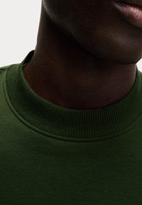 Felpa nera in cotone con collo a crew e tessuto liscio, che mostra i dettagli del collo e del tessuto.