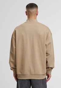 Beige sweatshirt met een hoge kraag, oversized fit en geribbelde manchetten. Gladde textuur, met minimale stiksels op de achterkant.
