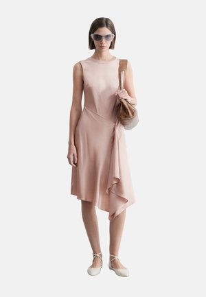 Kobieta w różowej asymetrycznej sukience bez rękawów, białych balerinach, dużych okularach przeciwsłonecznych i z brązową skórzaną torebką na ramię.