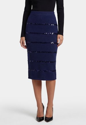 Donna che indossa una gonna a tubino blu navy al ginocchio con strisce orizzontali di paillettes, abbinata a tacchi alti neri e un top nero a maniche lunghe.