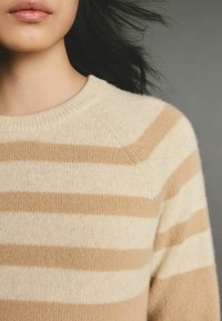 Pull en laine douce mélangée, beige et crème, avec un col rond et un léger détail à côtes au niveau du col et de l'ourlet.