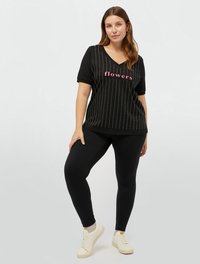 Tricou scurt cu mânecă, de culoare neagră, cu decolteu în V, având text „flori” în roz și țepi metalici argintii, asortat cu colanți negri și adidași albi.