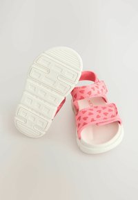 Rosa sandaler med hjärtmönster, vita sulor, justerbara remmar och texturerad fotbädd. Designade för komfort och avslappnad användning.