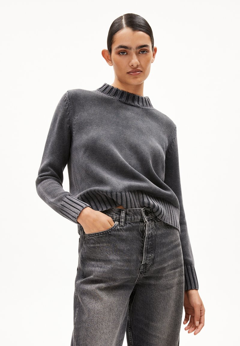 Grauer Strickpullover mit geripptem Rundhalsausschnitt und Bündchen, kombiniert mit hochtaillierten grauen Jeans, die eine lockere Passform und eine weiche Textur zeigen.