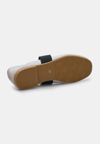 Scarpa piatta con tomaia in pelle bianca, cinturino nero e suola in gomma marrone con motivo di grip testurizzato. Taglia contrassegnata come 37.